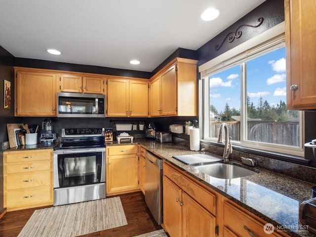 kitchen with dark wood-type flooring, recessed lighting, dark stone countertops, appliances with stainless steel finishes, and a sink