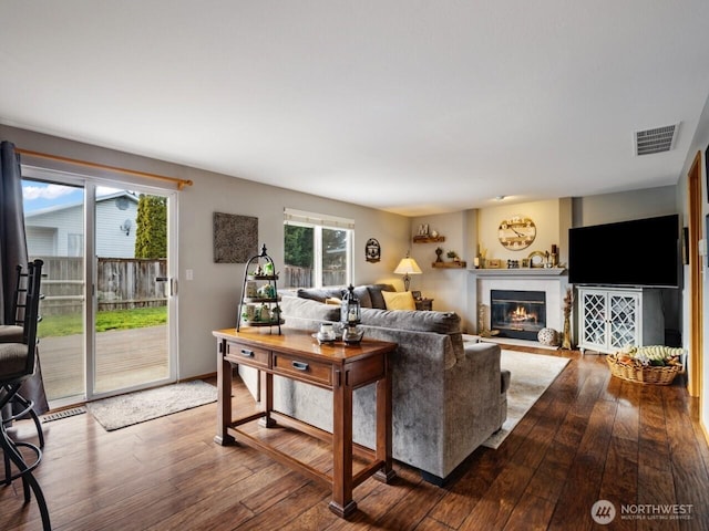 living room featuring visible vents, baseboards, a glass covered fireplace, and hardwood / wood-style floors