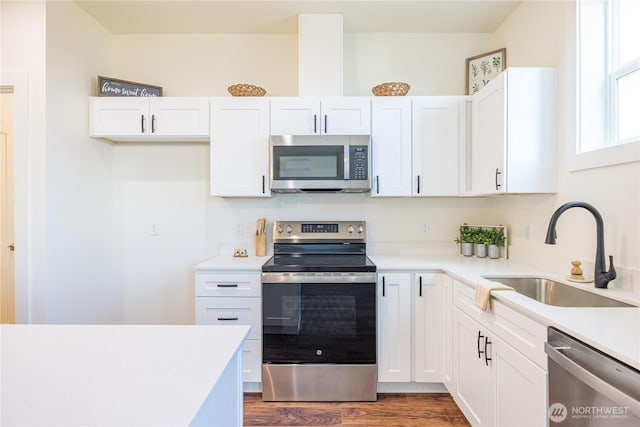 kitchen with wood finished floors, stainless steel appliances, light countertops, white cabinetry, and a sink