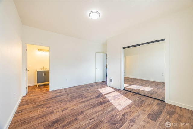 unfurnished bedroom with a closet, wood finished floors, visible vents, and baseboards