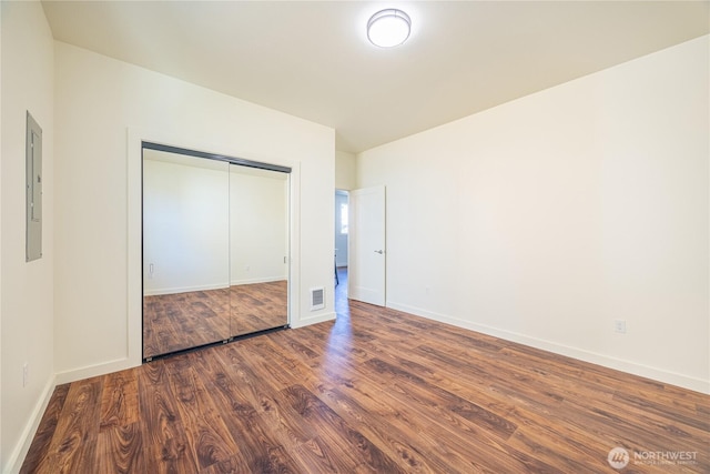 unfurnished bedroom with a closet, electric panel, baseboards, and wood finished floors