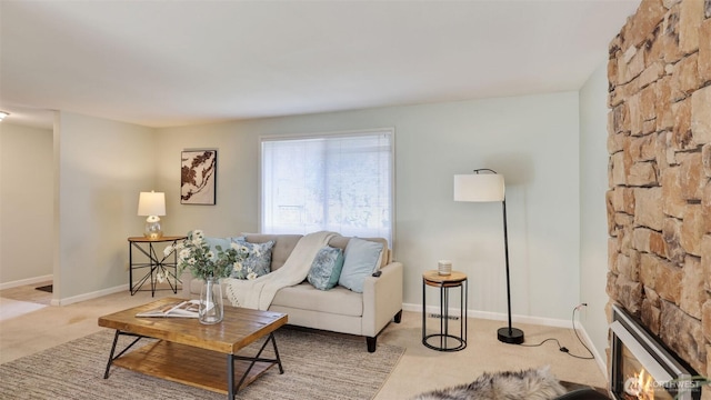 carpeted living area featuring a stone fireplace and baseboards