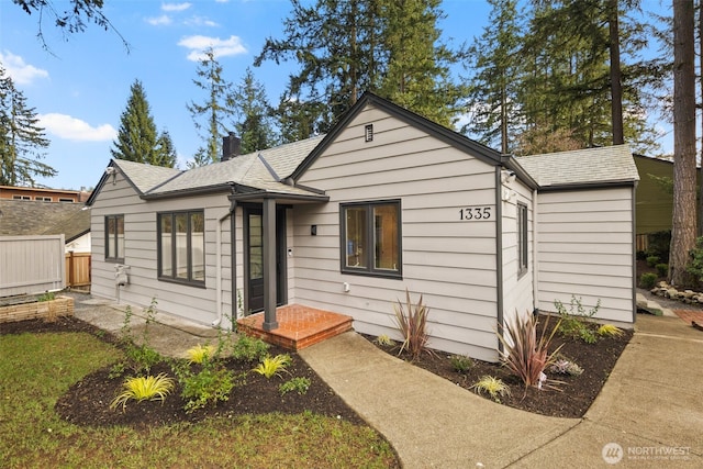 bungalow featuring a chimney, fence, and roof with shingles