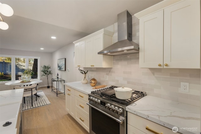 kitchen with light wood-style flooring, white cabinetry, wall chimney range hood, high end range, and decorative backsplash