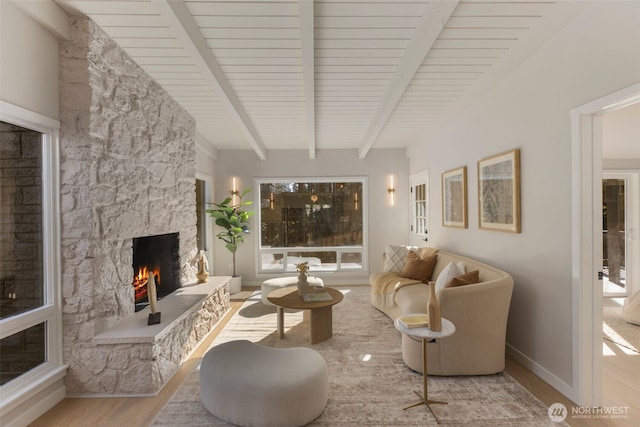 living room with beamed ceiling, a stone fireplace, baseboards, and wood finished floors