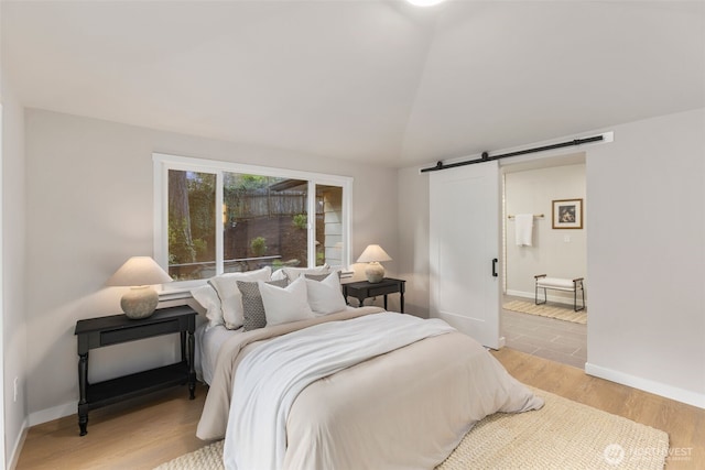 bedroom with light wood finished floors, a barn door, and baseboards