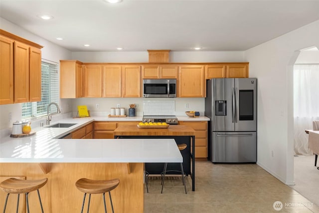 kitchen featuring arched walkways, appliances with stainless steel finishes, light countertops, and a sink