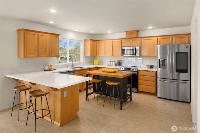 kitchen with appliances with stainless steel finishes, a kitchen breakfast bar, a peninsula, light countertops, and a sink