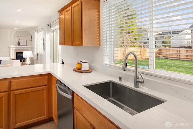 kitchen featuring light stone counters, a fireplace, stainless steel dishwasher, open floor plan, and a sink