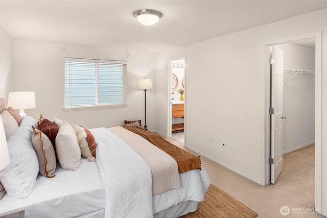 bedroom featuring light colored carpet, baseboards, a spacious closet, a closet, and ensuite bath