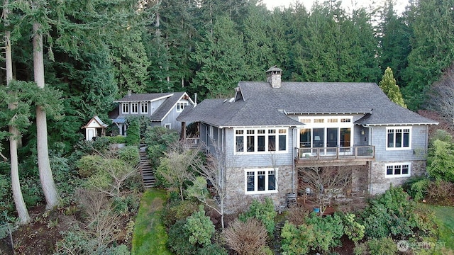 rear view of house with a shingled roof, stairs, cooling unit, a chimney, and stone siding