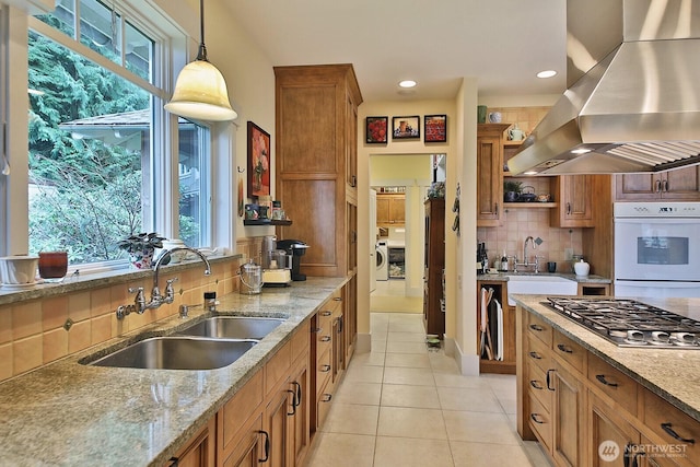 kitchen with a sink, brown cabinets, range hood, and stainless steel gas cooktop