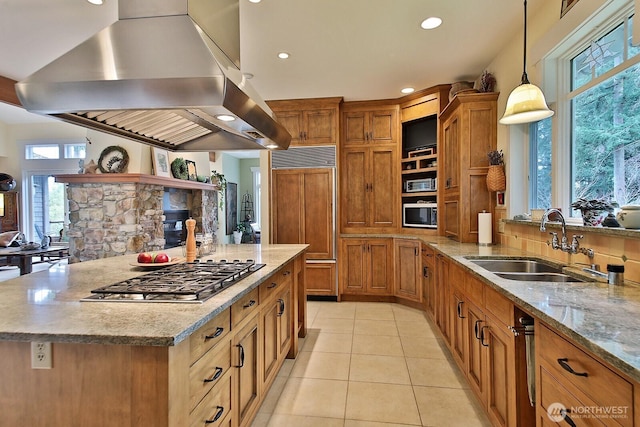 kitchen featuring light tile patterned floors, brown cabinetry, stainless steel gas cooktop, island exhaust hood, and a sink