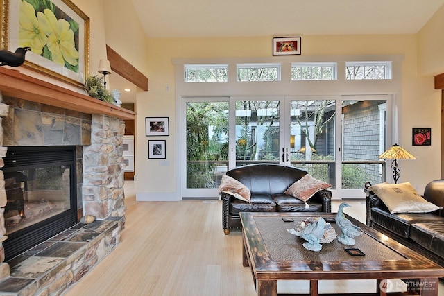 living room featuring a stone fireplace, baseboards, and light wood-style floors