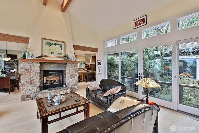 living area with visible vents, beam ceiling, high vaulted ceiling, wood finished floors, and a stone fireplace