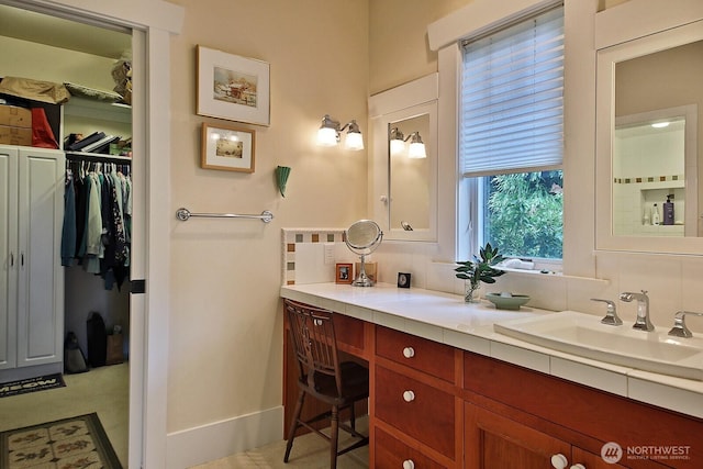 full bath featuring decorative backsplash, vanity, a walk in closet, and baseboards