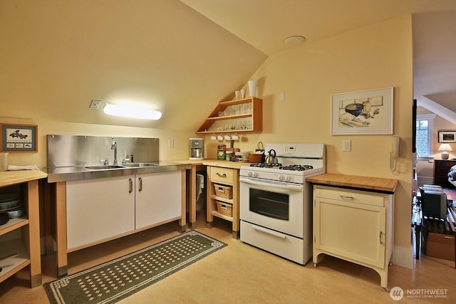 kitchen featuring open shelves, white range with gas stovetop, a sink, vaulted ceiling, and stainless steel counters