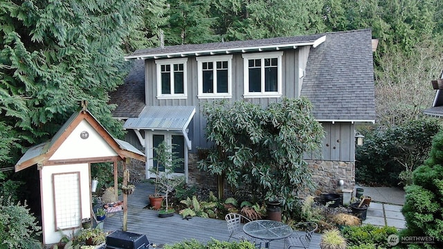 view of front of home with stone siding, roof with shingles, board and batten siding, and a deck