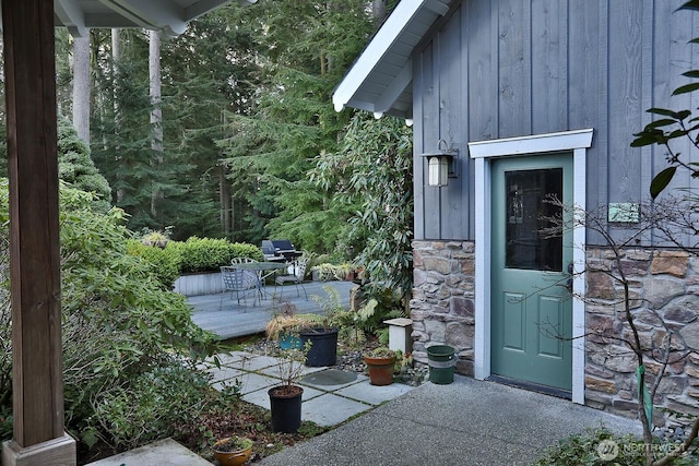 doorway to property with a deck, board and batten siding, and stone siding