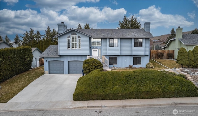 bi-level home with a garage, fence, concrete driveway, a front lawn, and a chimney