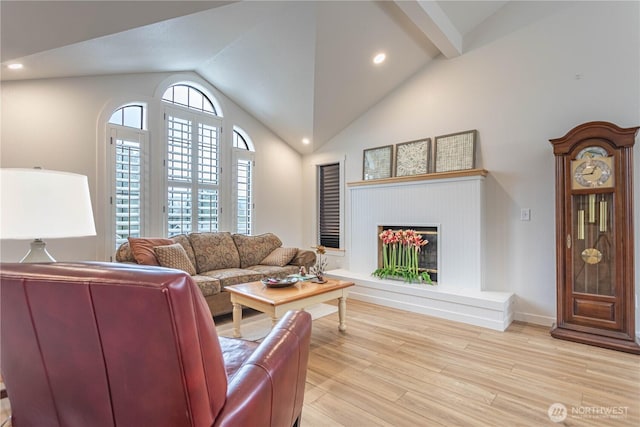 living room with light wood finished floors, baseboards, a fireplace with raised hearth, vaulted ceiling, and recessed lighting