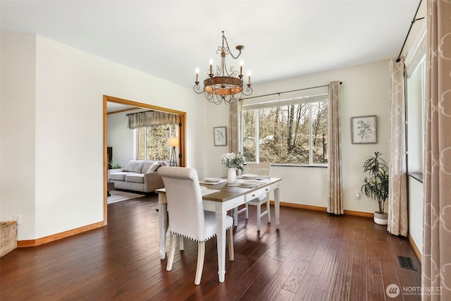 dining room with dark wood-type flooring, plenty of natural light, baseboards, and an inviting chandelier