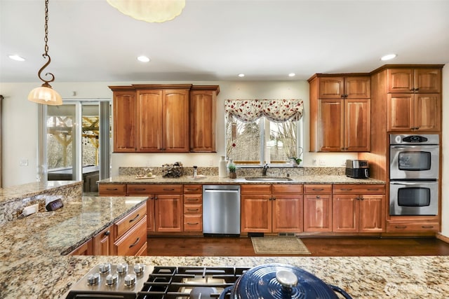 kitchen with recessed lighting, stainless steel appliances, a sink, hanging light fixtures, and light stone countertops