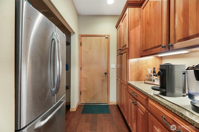 kitchen with light stone countertops, baseboards, freestanding refrigerator, brown cabinets, and dark wood finished floors