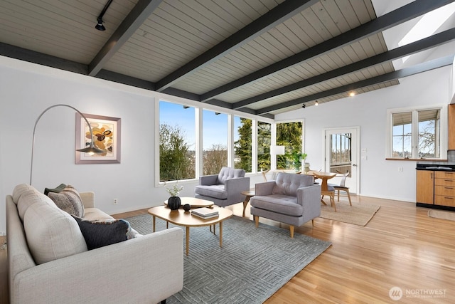 living area featuring rail lighting, plenty of natural light, light wood-type flooring, and vaulted ceiling with beams