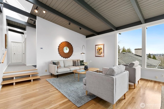 living area with baseboards, light wood-style floors, and vaulted ceiling with beams