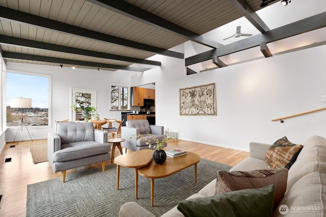 living room featuring visible vents, light wood-style flooring, baseboards, ceiling fan, and vaulted ceiling with beams