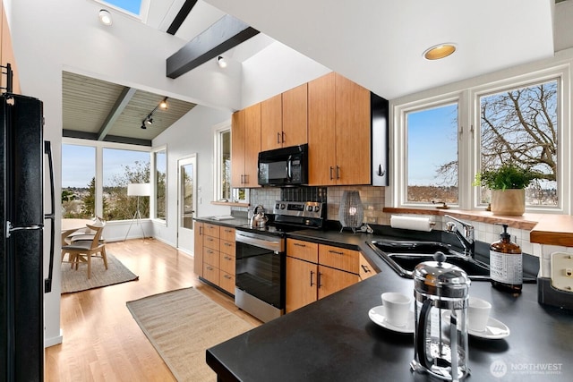 kitchen with dark countertops, backsplash, vaulted ceiling with beams, black appliances, and a sink