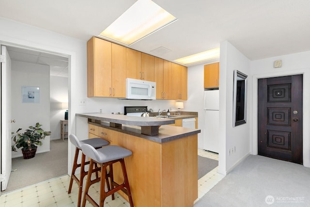 kitchen featuring a sink, white appliances, a peninsula, a breakfast bar area, and light floors