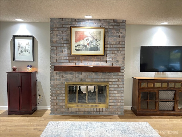 living area featuring a textured ceiling, a fireplace, wood finished floors, and baseboards