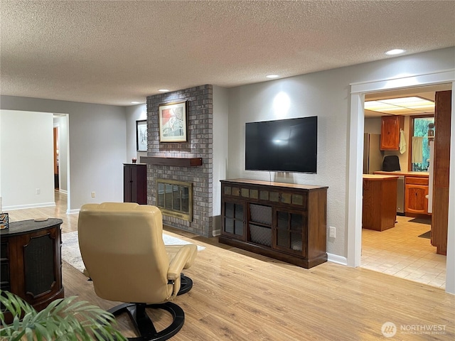 living area with baseboards, a fireplace, a textured ceiling, and light wood finished floors