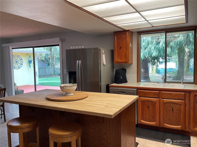 kitchen with a sink, butcher block counters, a kitchen bar, and stainless steel fridge