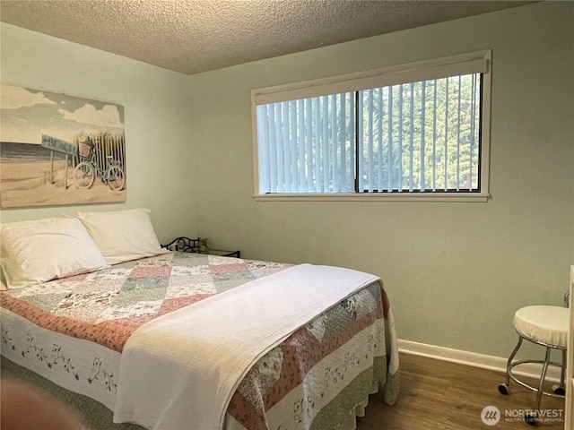 bedroom with a textured ceiling, baseboards, and wood finished floors