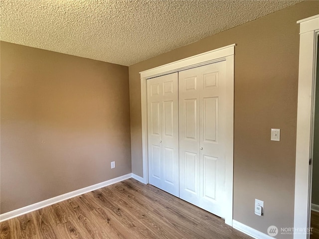 unfurnished bedroom featuring a textured ceiling, a closet, baseboards, and wood finished floors