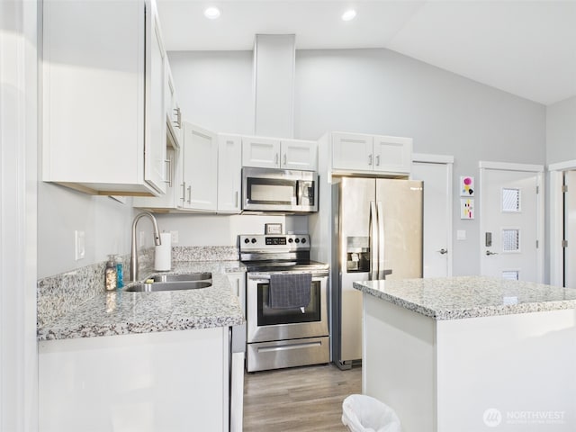 kitchen with stainless steel appliances, lofted ceiling, light wood-style flooring, white cabinetry, and a sink