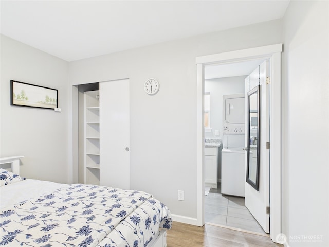 bedroom featuring stacked washer and dryer, baseboards, a closet, light wood-type flooring, and ensuite bath