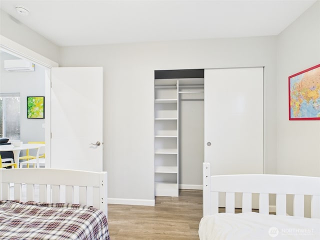 bedroom with a closet, a wall mounted AC, wood finished floors, and baseboards