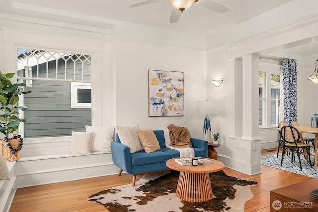 living area featuring ceiling fan, baseboards, ornate columns, and wood finished floors