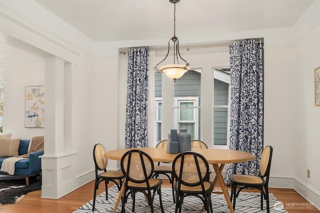 dining space with decorative columns, wood finished floors, and baseboards