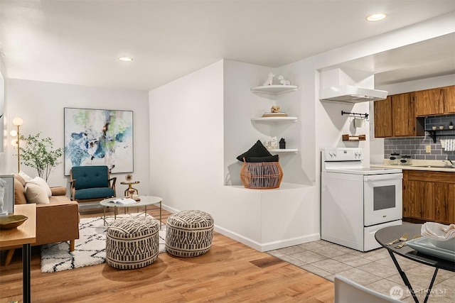 kitchen with backsplash, wall chimney range hood, light countertops, brown cabinets, and white electric range