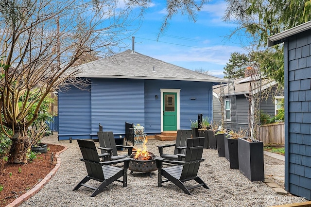 rear view of house featuring fence, a fire pit, entry steps, and a shingled roof