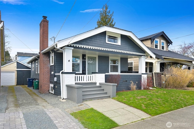 view of front facade featuring driveway, a chimney, a detached garage, an outbuilding, and a porch