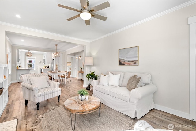 living room with ornamental molding, a ceiling fan, light wood-style flooring, and baseboards