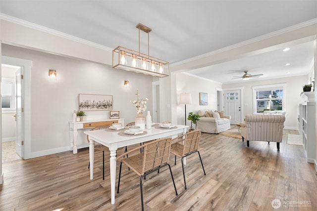 dining area with light wood-type flooring, a ceiling fan, baseboards, and crown molding