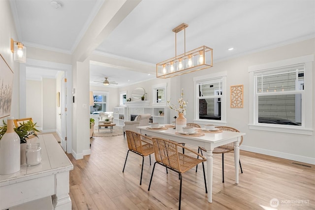 dining area with visible vents, light wood-style floors, ornamental molding, a tile fireplace, and baseboards