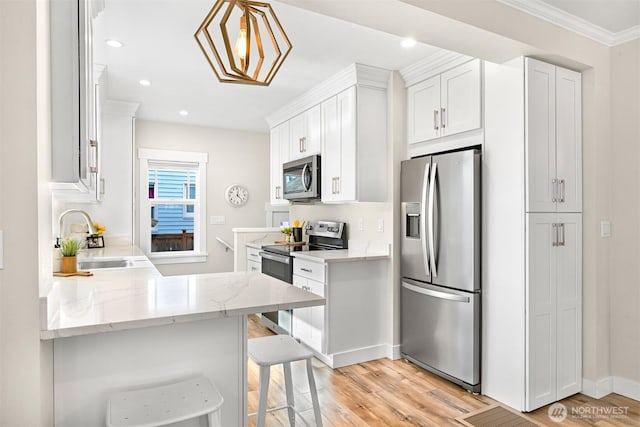 kitchen with white cabinets, light stone counters, a breakfast bar area, appliances with stainless steel finishes, and a sink